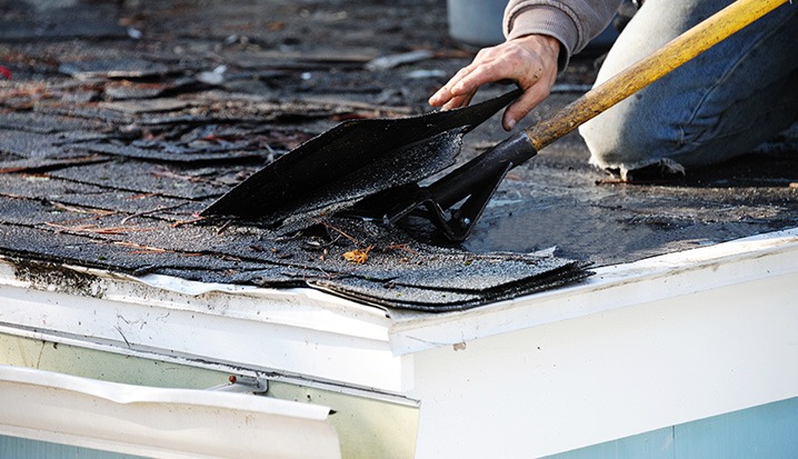 A person uses a shovel to remove old, damaged shingles from a roof during a repair or replacement project by a New Orleans Roofing Company.
