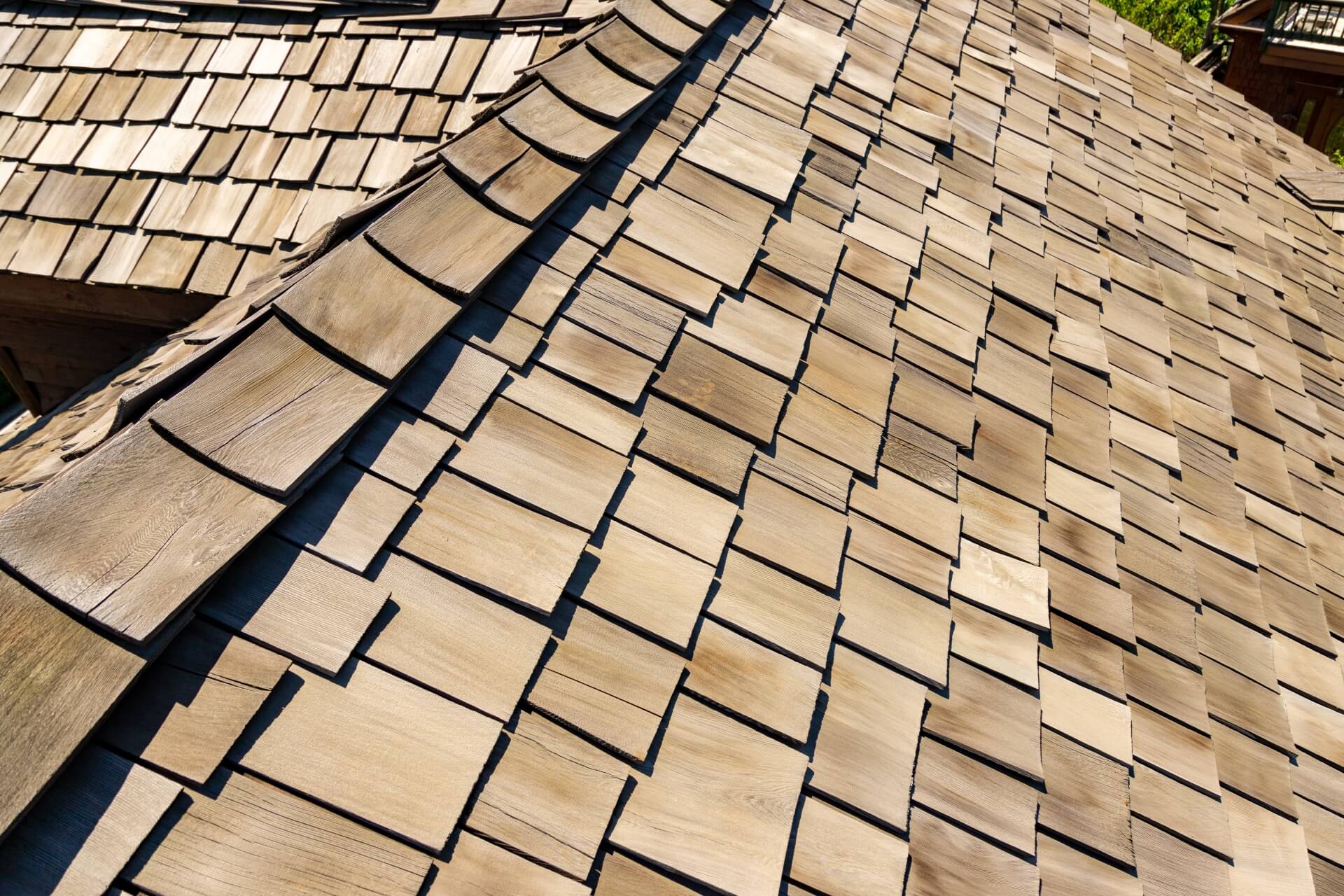 Close-up view of a roof covered with overlapping cedar shake shingles, laid in an overlapping pattern. The light brown wood appears weathered, creating a natural and textured surface.