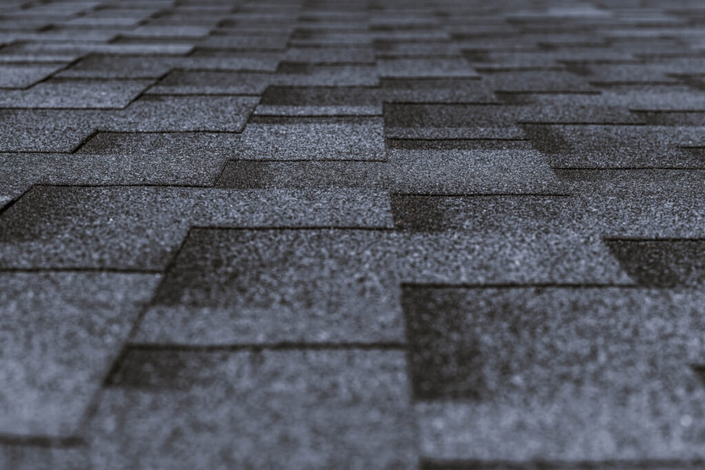 Close-up view of gray asphalt roof shingles arranged in a uniform, overlapping pattern, showcasing the textured surface typical of New Orleans Shingle Roofing as it gradually blurs into the distance.