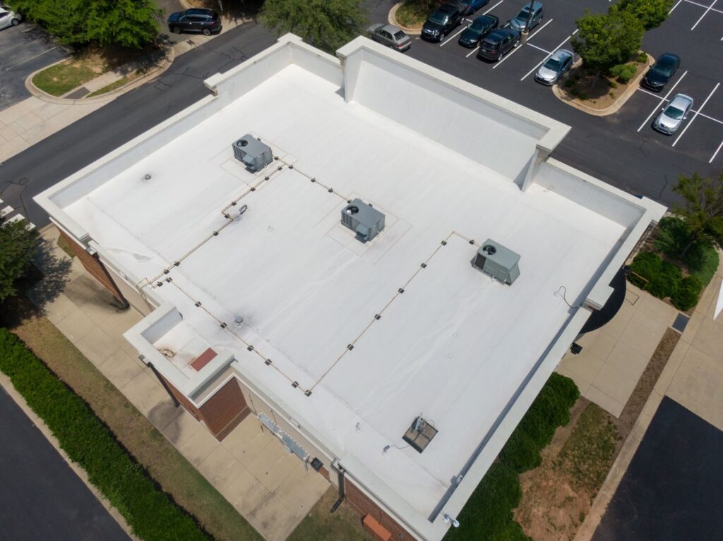 Aerial view of a white flat-roofed building with three rooftop HVAC units, showcasing a recent roof replacement in New Orleans, surrounded by parking lots, trees, and sidewalks.