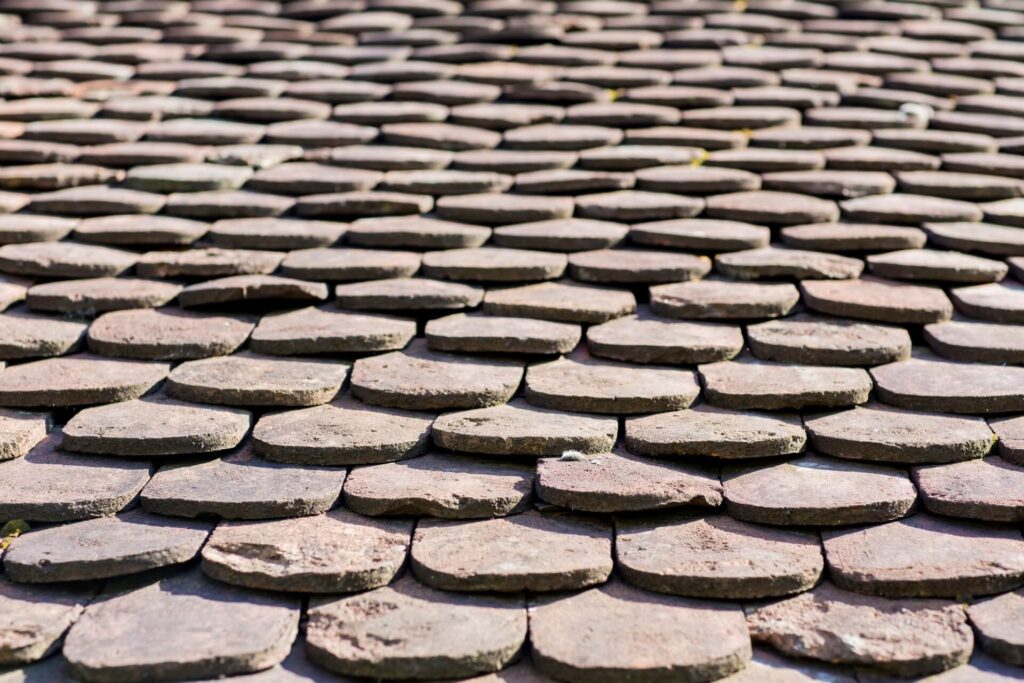 Close-up view of overlapping rows of weathered, rounded stone roof tiles, creating a textured and repeating pattern reminiscent of classic New Orleans shingle roofing.