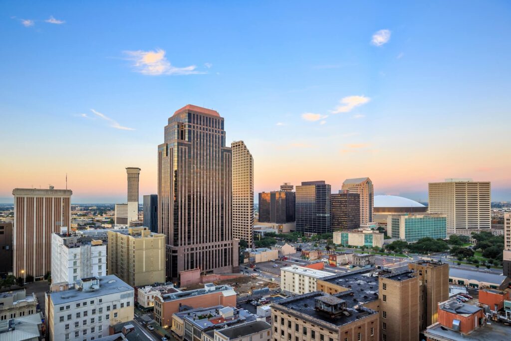 Downtown city skyline at sunset with tall office buildings, a mix of modern and historic architecture, and clear skies—a stunning view that highlights the need for reliable commercial roof coating in New Orleans.