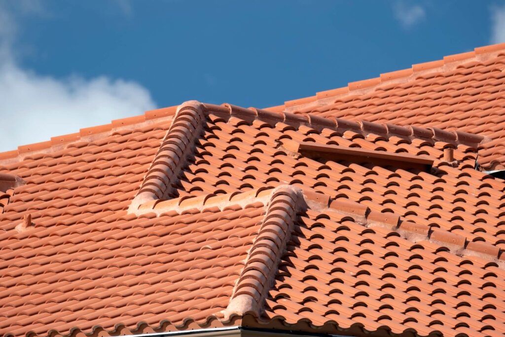 A close-up of a red clay tiled roof with multiple intersecting slopes and ridges, showcasing classic New Orleans Tile Roofing, set against a blue sky with a few clouds.