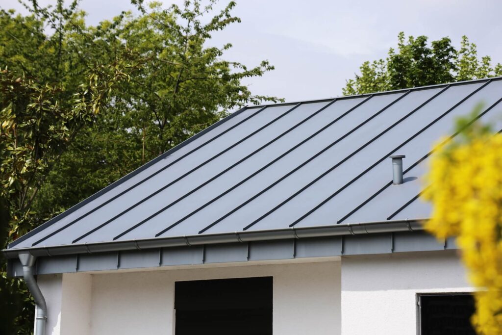 A modern house with a grey metal standing seam roof by Metal Roofing New Orleans, surrounded by green trees and a blurred yellow plant in the foreground.